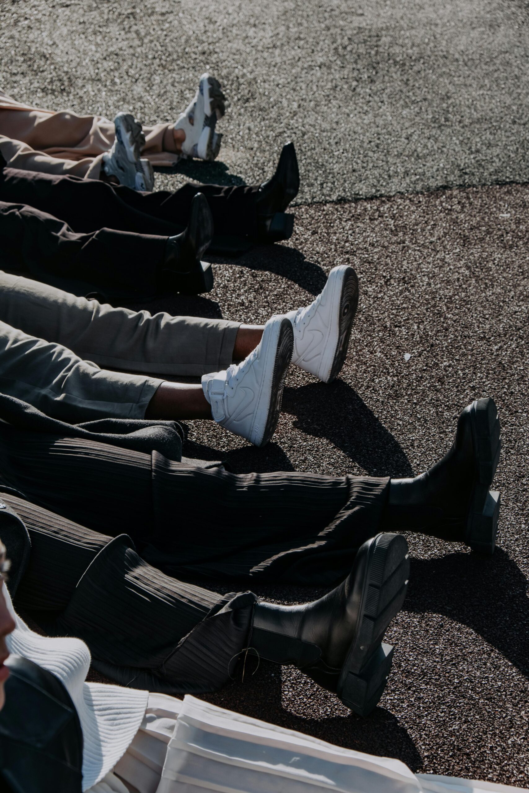 Group of people sitting on pavement wearing boots and sneakers, casual street style footwear